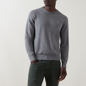 Model wearing Gant Classic Shield Sweater in dark grey melange, crew neck with ribbed trims and embroidered logo, styled with dark green trousers.