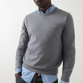 Model wearing Gant Classic Shield Sweater in dark grey melange, crew neck with ribbed trims and embroidered logo, styled over light blue shirt.