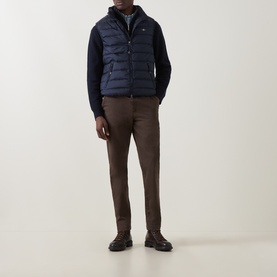 Model wearing Gant Evening Blue quilted gilet over navy knit sweater, with brown trousers and dark leather shoes.