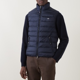 Model wearing Gant Evening Blue quilted down gilet with zip front, styled with navy knit sleeves and brown trousers.
