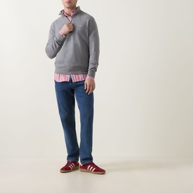 Model wearing Gant Shield Logo Half-Zip Sweatshirt in dark grey melange, styled with pink stripe shirt, blue jeans, and red trainers.
