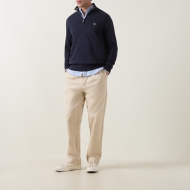 Model wearing Gant Shield Logo Half-Zip Sweatshirt in Evening Blue with beige chinos and white trainers.
