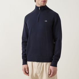 Model wearing Gant Shield Logo Half-Zip Sweatshirt in Evening Blue, funnel neck with quarter zip, small shield logo. Styled with cream trousers.