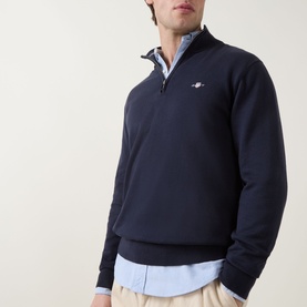 Model wearing Gant Shield Logo Half-Zip Sweatshirt in Evening Blue with funnel neck, styled over a light blue shirt with chinos.