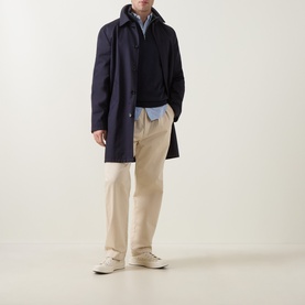 Model wearing Gant Shield Logo Half-Zip Sweatshirt in Evening Blue with navy overcoat, styled with beige trousers and white trainers.