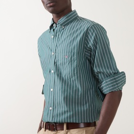 Model wearing Gant Reg Shirt in dark emerald with white vertical stripes, chest pocket, button-down collar, sleeves rolled up, styled with chinos.