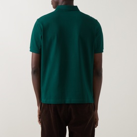 Model wearing Gant Regular Polo in dark emerald, rear view, short sleeves, piqu&eacute; cotton, styled with brown cord trousers.