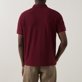 Model wearing Gant Regular Polo in deep grape wine, piqu&eacute; cotton, short sleeves, rear view, styled with beige trousers.