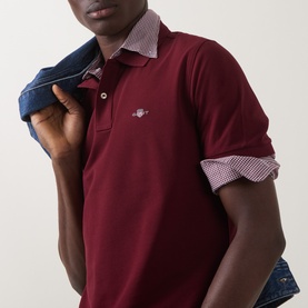 Model wearing Gant Regular Polo in deep grape wine, short sleeves, with contrast gingham collar lining, paired with denim jacket.