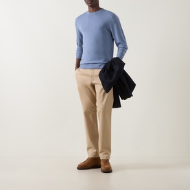 Model wearing Canali Fine-Knit Sweater in light blue crew neck, styled with beige chinos and brown suede shoes, holding navy jacket.