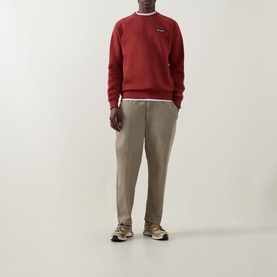 Model wearing Columbia crew neck sweatshirt in Red Oxide, styled with beige tapered trousers and retro trainers.