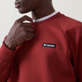 Model wearing Columbia Red Oxide crew neck sweatshirt with small logo patch, styled with a white crew neck underneath.