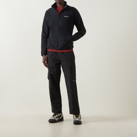 Model wearing Columbia Pacific Arch Logo 200 Zip Fleece Jacket in black, styled with black trousers and hiking boots.