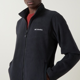 Model wearing Columbia Pacific Arch Logo 200 Zip Fleece Jacket in black, with white logo detail, full zip fastening and side pockets, styled over red