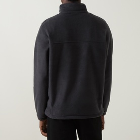 Model wearing Columbia black fleece pullover, rear view, showing back seam detail and high collar, styled with black trousers