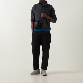 Model wearing Columbia black fleece half-zip pullover with small crossbody bag, styled with black joggers and grey trainers.