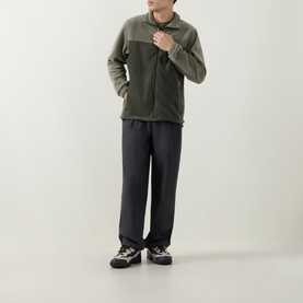 Model wearing Columbia Stone Green fleece jacket with dark tailored trousers and grey trail trainers.