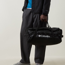 Model carrying Columbia Landroamer&trade; 40L Holdall Bag in black, with multiple haul handles and logo branding, styled with black jacket and trousers.