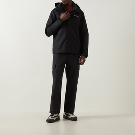 Model wearing Columbia black hooded zip-up jacket with black cargo trousers and grey trail trainers.
