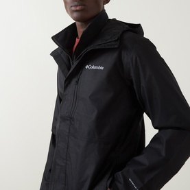 Model wearing Columbia black hooded waterproof jacket, close-up showing chest logo, zip fastening and storm collar detail.