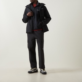 Model wearing Columbia black hooded jacket with matching dark trousers, red top visible at collar, and grey hiking trainers.