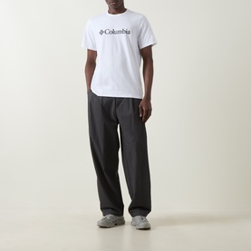 Model wearing Columbia CSC Basic Logo T-Shirt in white with chest logo, styled with dark wide-leg trousers and grey trainers.