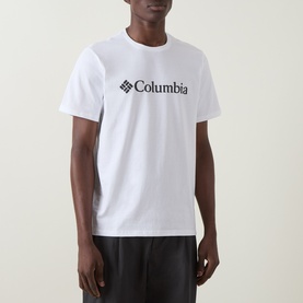 Model wearing Columbia CSC Basic Logo T-Shirt in white, round neck with front logo print, paired with dark trousers.