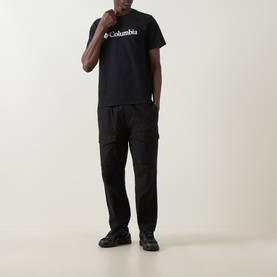 Model wearing Columbia CSC Basic Logo T-Shirt in black, styled with black cargo trousers and dark trainers.