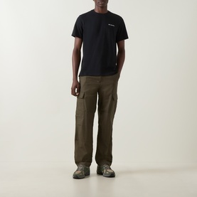 Model wearing Columbia CSC Logo Back Graphic T-Shirt in black, styled with olive cargo trousers and grey hiking shoes.