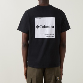 Model wearing Columbia CSC Logo Back Graphic T-Shirt in black, showing large back logo graphic print, styled with olive cargo trousers.