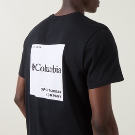Model wearing Columbia CSC Logo Back Graphic T-Shirt in black, showing rear white square logo graphic print on 100% cotton tee.