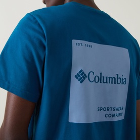 Model wearing Columbia CSC Logo Back Graphic T-Shirt in Phoenix Blue, showing back graphic with Columbia Sportswear Company logo print.