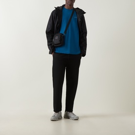 Model wearing Columbia CSC Logo Back Graphic T-Shirt in Phoenix Blue with black zip-up jacket, black trousers, and grey trainers.
