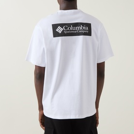 Model wearing Columbia white T-shirt, back view showing large black branded logo graphic print, 100% cotton crew neck tee.