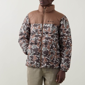 Model wearing Columbia puffer jacket in Fossil brown and camo print, zip-up high collar, paired with khaki trousers