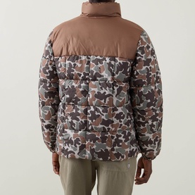 Model wearing Columbia puffer jacket in Fossil and camo print, rear view, with khaki trousers. Quilted panels, high collar.