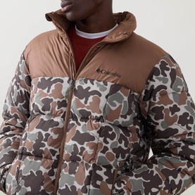 Model wearing Columbia puffer jacket in Fossil and camo print, brown yoke panel, zip front, styled with red crew neck top