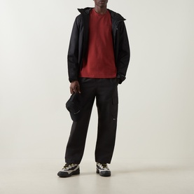 Model wearing Columbia Red Oxide cotton T-shirt, styled with black zip-up jacket, black cargo trousers, and multicolour trainers.