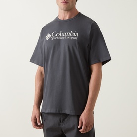 Model wearing Columbia CSC Retro Logo T-Shirt in Shark grey, featuring crew neck and white chest logo print, paired with grey trousers.