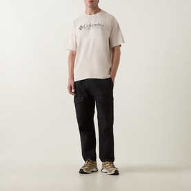 Model wearing Columbia CSC Retro Logo T-Shirt in Dark Stone, styled with black cargo trousers and tan trainers.