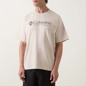 Model wearing Columbia CSC Retro Logo T-Shirt in Dark Stone, round neck, short sleeves, chest logo print, paired with black trousers.