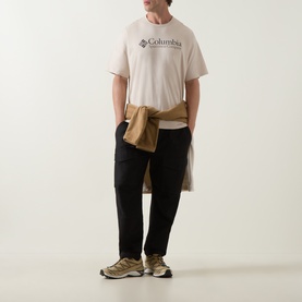 Model wearing Columbia CSC Retro Logo T-Shirt in Dark Stone, styled with black trousers and beige trainers, jacket tied at waist.