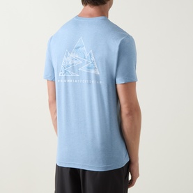 Model wearing Columbia Parons Logo Back Graphic T-Shirt in Rainy Day Heather blue, back view showing mountain graphic print, with black shorts.