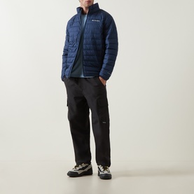 Model wearing Columbia Parons Logo Back Graphic T-Shirt in Rainy Day Heather, styled with navy quilted jacket and black cargo trousers.