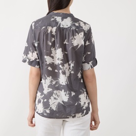 Model wearing Marc O Polo blouse in dark grey floral print, short rolled sleeves, back view, styled with white trousers