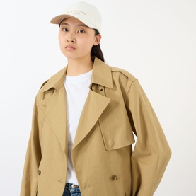 Model with Marc O Polo Modern Logo Cap in White Cotton, curved visor, embroidered logo. Styled with a camel trench coat and white tee.