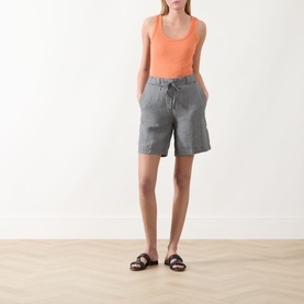 Model wearing Marc O Polo Woven Linen Shorts in Slate Grey Melange with drawstring waist, styled with an orange tank top and brown sandals.