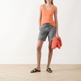 Model wearing Marc O Polo Woven Linen Shorts in Slate Grey Melange with orange tank top and black slide sandals, holding coral knit