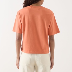 Model wearing Marc O Polo Warm Orange oversized cotton-modal T-shirt, back view, styled with cream wide-leg trousers.