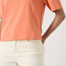 Model wearing Marc O Polo warm orange relaxed-fit T-shirt, styled with cream wide-leg trousers. Close-up torso shot.